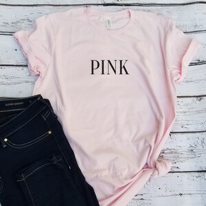 May include: A pink t-shirt with the word "PINK" printed in black on the front.