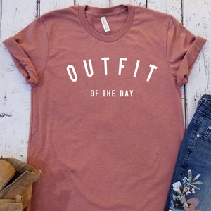 May include: A maroon t-shirt with the text "OUTFIT OF THE DAY" in white.