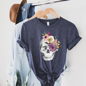 May include: A navy blue t-shirt with a white skull graphic. The skull is adorned with a floral crown of pink, yellow, and purple flowers.