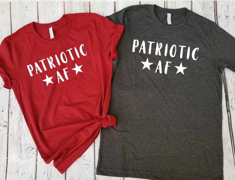 May include: Two t-shirts with the text "PATRIOTIC AF" and stars printed on them. The shirt on the left is red and the shirt on the right is gray.