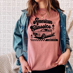 Puede incluir: Una camiseta rosa con un gr&aacute;fico negro de un coche cl&aacute;sico y el texto "American Classics Summer Cruise".