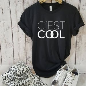 May include: Black t-shirt with white text that reads "C'est Cool" with the "O"s replaced with interlocking circles.