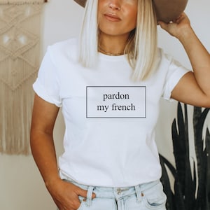 Puede incluir: Camiseta blanca con el texto "pardon my french" impreso en negro dentro de un rectángulo.