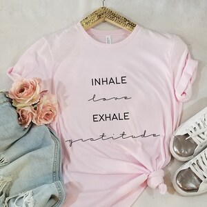 May include: Pink t-shirt with the text "INHALE love EXHALE gratitude" written in black.