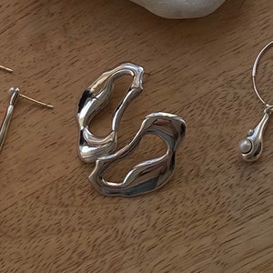 A pair of silver earrings with a unique abstract design. The earrings are made of smooth, shiny silver and have a modern, minimalist style. The earrings are displayed on a wooden surface.
