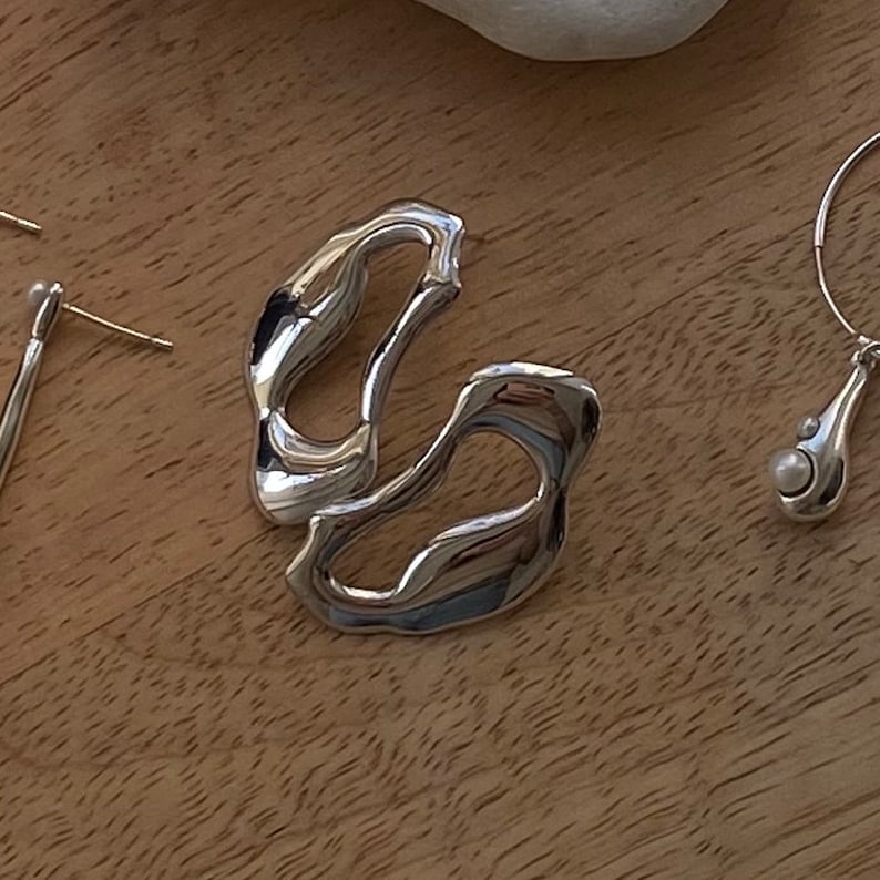 A pair of silver earrings with a unique abstract design. The earrings are made of smooth, shiny silver and have a modern, minimalist style. The earrings are displayed on a wooden surface.
