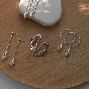 A set of silver earrings with pearl accents. The earrings are displayed on a wooden surface with a white stone.
