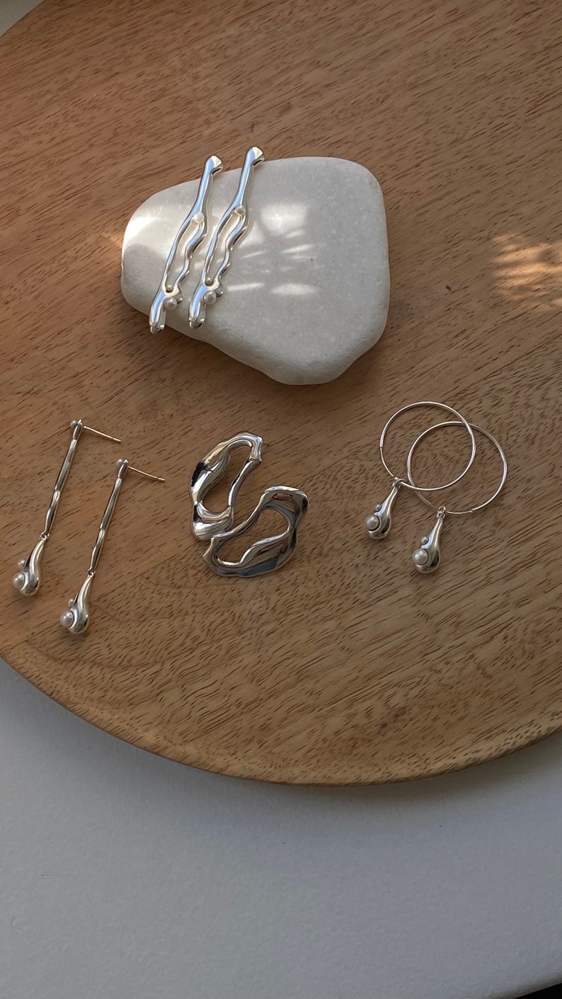 A set of silver earrings with pearl accents. The earrings are displayed on a wooden surface with a white stone.