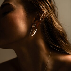 A pair of silver abstract earrings with a smooth, organic shape.