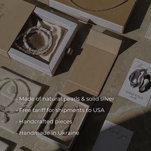 Pu&ograve; includere: Un assortimento di gioielli, tra cui collane, bracciali e orecchini, presentati in eleganti scatole e sacchetti. L'immagine presenta il marchio "ANNA KOVA" e il testo "Made of natural pearls & solid silver".