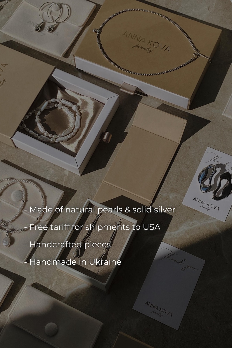 Pu&ograve; includere: Un assortimento di gioielli, tra cui collane, bracciali e orecchini, presentati in eleganti scatole e sacchetti. L'immagine presenta il marchio "ANNA KOVA" e il testo "Made of natural pearls & solid silver".