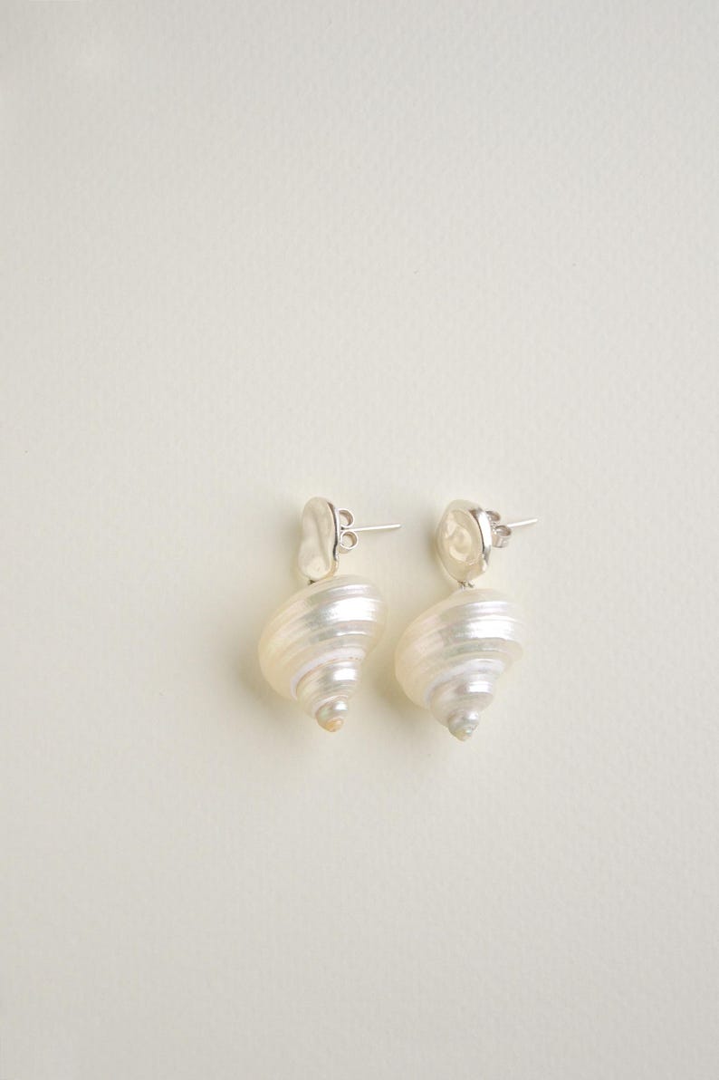 Pu&ograve; includere: Un paio di orecchini con un design a conchiglia a spirale. Gli orecchini hanno un perno d'argento e un colore bianco sporco perlescente. Un accessorio unico.