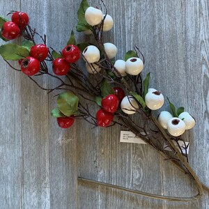 May include: A sprig of artificial berries with red and white berries. The berries are clustered together on a brown stem with green leaves.
