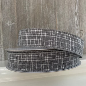 May include: Gray and white plaid ribbon with a woven texture. The ribbon is rolled up on a spool.