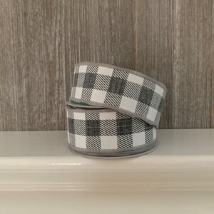 May include: Two rolls of black and white buffalo plaid ribbon. The ribbon is made of a woven fabric and has a slightly textured surface.