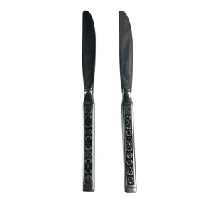 Op de afbeelding: Twee zilveren botermesjes met sierlijke ontwerpen op de handvatten.