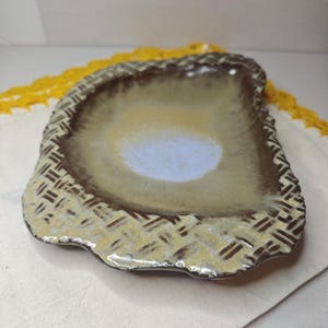 Könnte beinhalten: Eine Keramik-Servierschale mit einer einzigartigen, organischen Form. Die Schale hat eine hellblaue Mitte, umgeben von einem Farbverlauf aus Beige und Braun. Der Rand hat ein strukturiertes, gewebtes Muster in Beige- und Brauntönen.