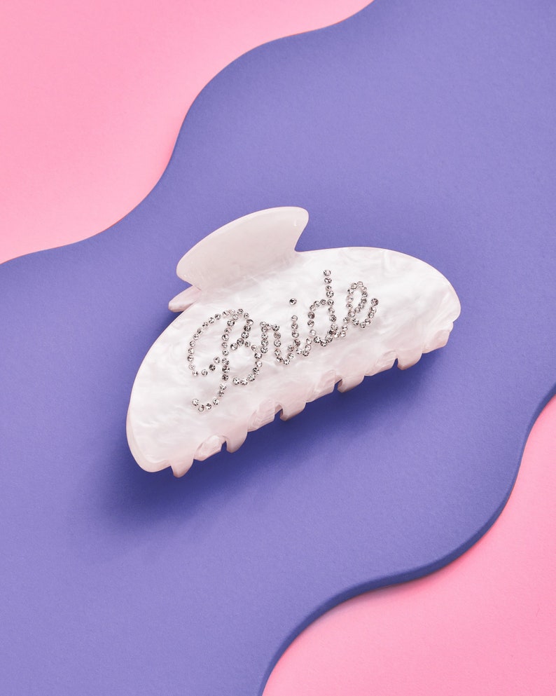 K&ouml;nnte beinhalten: Wei&szlig;er Plastik-Haarklammer mit dem Wort "Bride" in Strasssteinen.