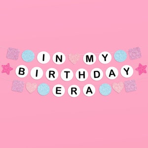 May include: A pink and blue birthday banner with the words "It's My Birthday Era" in white letters on a white background.