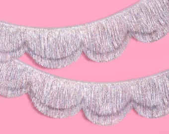 May include: Two rows of iridescent silver fringe trim arranged in a scalloped pattern. The fringe consists of thin, reflective metallic strands that catch the light, creating a shimmering effect across the curved, layered edges of the material.