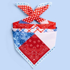 May include: A folded bandana with a patchwork design in red, white, and blue. The bandana features various patterns, including gingham, paisley, floral, and geometric shapes. The bandana is tied at the top with the ends forming a bow.