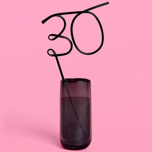 May include: A black metal straw bent into the shape of the number "30" and placed in a clear glass with a dark gray liquid.