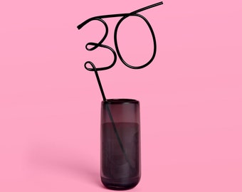 May include: A black metal straw bent into the shape of the number "30" and placed in a clear glass with a dark gray liquid.