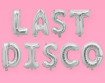 Op de afbeelding: Zilveren folie ballonnen die de zin "LAST DISCO" spellen tegen een roze achtergrond.