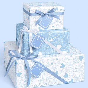 May include: Three gift boxes, stacked, wrapped in patterned paper with blue and white designs. Each box is tied with a ribbon and has a matching gift tag. The wrapping paper features hearts, bows, and floral patterns.