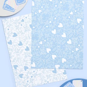 May include: A stationery set featuring light blue and white patterns. The set includes two sheets of paper with heart and bow designs, and several gift tags. The gift tags are light blue with a bow design and the word "Love".