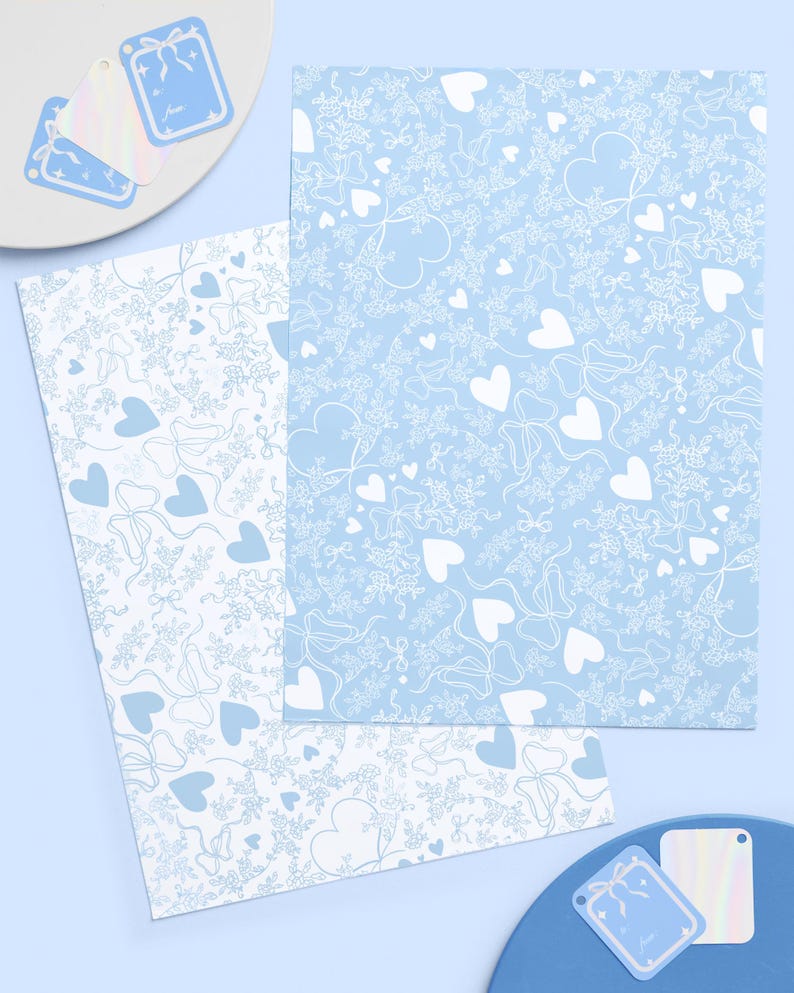 May include: A stationery set featuring light blue and white patterns. The set includes two sheets of paper with heart and bow designs, and several gift tags. The gift tags are light blue with a bow design and the word "Love".