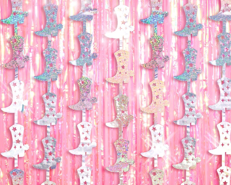 May include: A garland of iridescent silver and pink cowboy boots with stars on them. The boots are hanging on a pink and iridescent background.