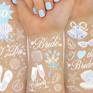 May include: Temporary tattoos with a bridal theme. Designs include seashells, starfish, wedding bells, and the words "I Do", "Bride", and "I love the Bride". The tattoos are in shades of white, blue, and iridescent.