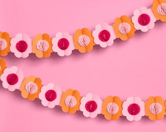 May include: A pink and orange paper flower garland with a honeycomb texture. The garland is made of paper flowers that are strung together.