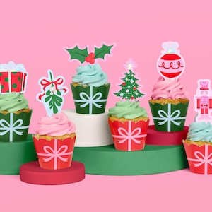 May include: A collection of festive cupcakes with various Christmas-themed toppers. The cupcakes have green and pink frosting, and are decorated with gift boxes, mistletoe, a Christmas tree, a bauble, and a nutcracker. The cupcake wrappers are red and green with white bows.