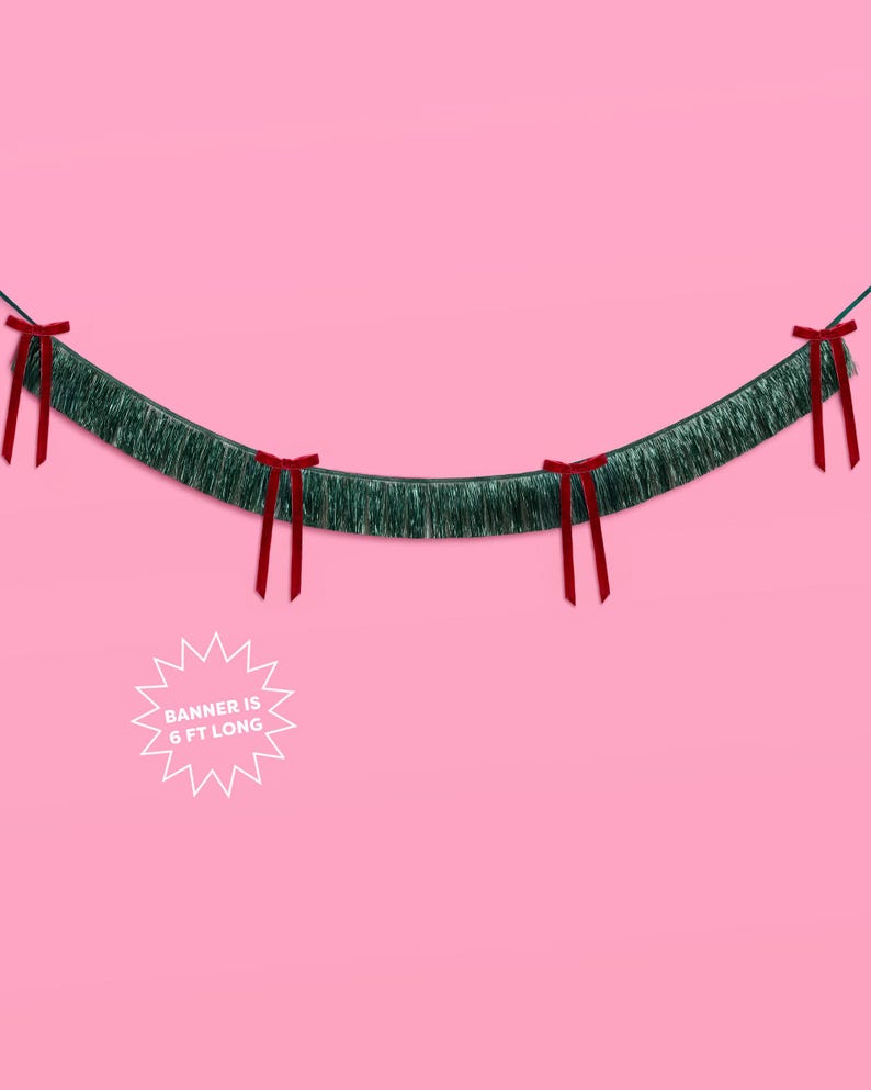 Puede incluir: Una guirnalda de oropel verde con lazos rojos, sobre un fondo rosa. La guirnalda mide 1,83 metros de largo, como indica el texto en un gr&aacute;fico de estrella blanca. El oropel tiene una textura de flecos.