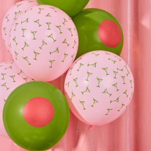 May include: A cluster of party balloons in shades of pink and green. Some pink balloons are patterned with small martini glass illustrations. Green balloons have a red circle design. The balloons are tied together with silver string.
