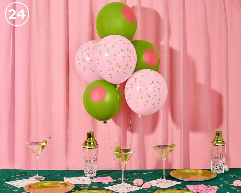 May include: A festive party scene with pink and green balloons, martini glasses, and gold-rimmed plates. The balloons are decorated with martini glass patterns and pink circles. The scene is set on a green tablecloth with a pink backdrop.