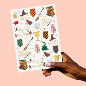 May include: A sheet of stickers featuring various wizard-themed illustrations. The stickers include a wizard hat, a golden trophy, a green snake, a frog, a broom, and the text "I'M A+ WIZARD" and "WIZARD IN TRAINING".