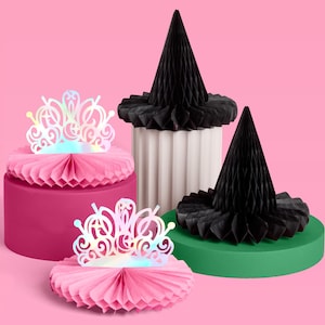 May include: A collection of party decorations on a pink background. The decorations include two black cone-shaped hats, two paper tiaras, and two round, pleated paper bases in pink and green. The tiaras have an iridescent finish.
