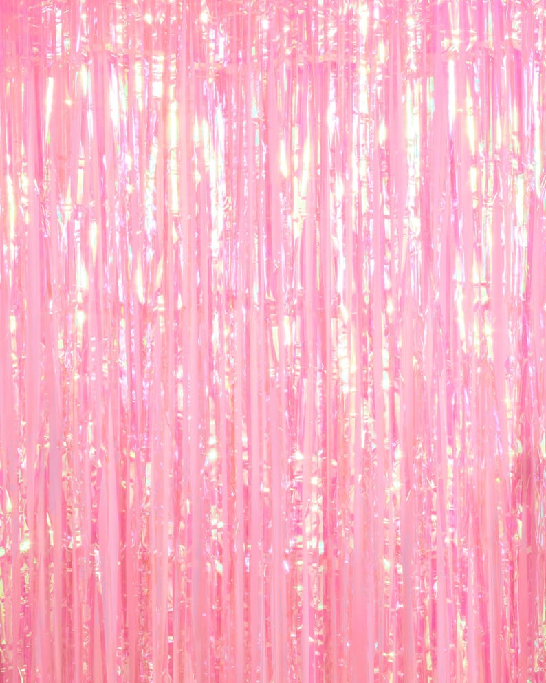 May include: A pink iridescent foil fringe curtain. The curtain is made of thin strips of foil that hang down in a vertical pattern. The foil is shiny and reflects light, creating a shimmering effect.