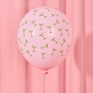 May include: A pink balloon with a pattern of green martini glasses. The balloon is inflated and tied with a string, set against a pink backdrop. This festive balloon is suitable for a party or celebration.
