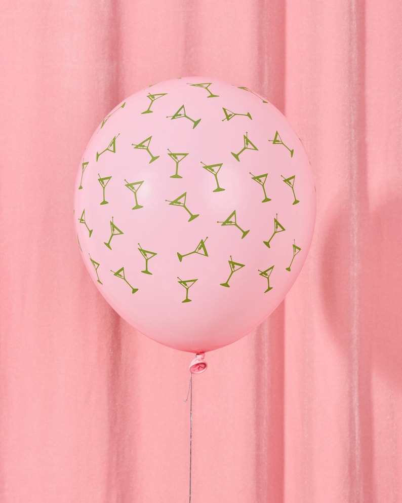 May include: A pink balloon with a pattern of green martini glasses. The balloon is inflated and tied with a string, set against a pink backdrop. This festive balloon is suitable for a party or celebration.