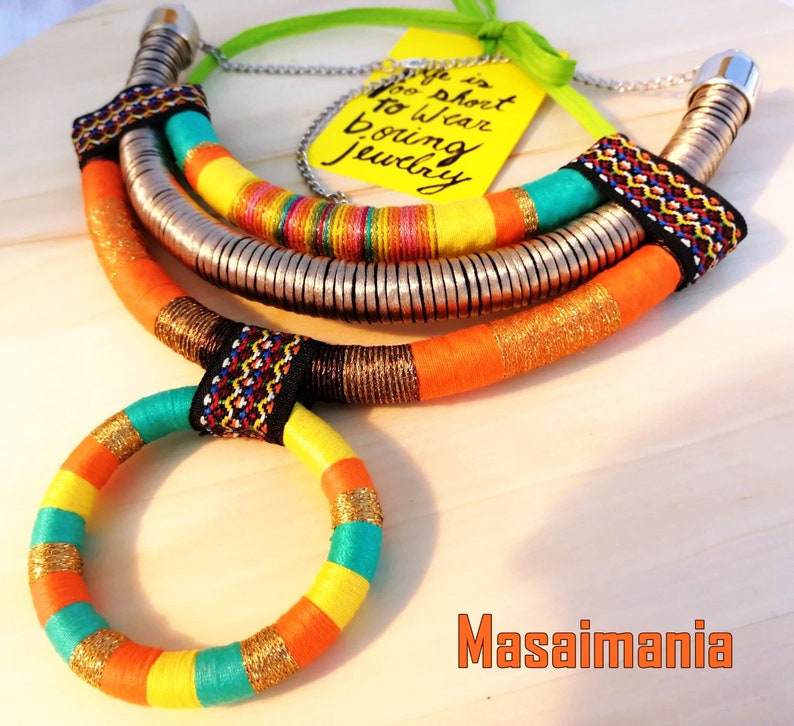 May include: A colorful multi-strand necklace with a silver chain and a circular pendant. The necklace is made of woven fabric and has a bright orange, yellow, turquoise, and black color scheme. The text "Life is too short to wear boring jewelry" is written on a yellow tag.