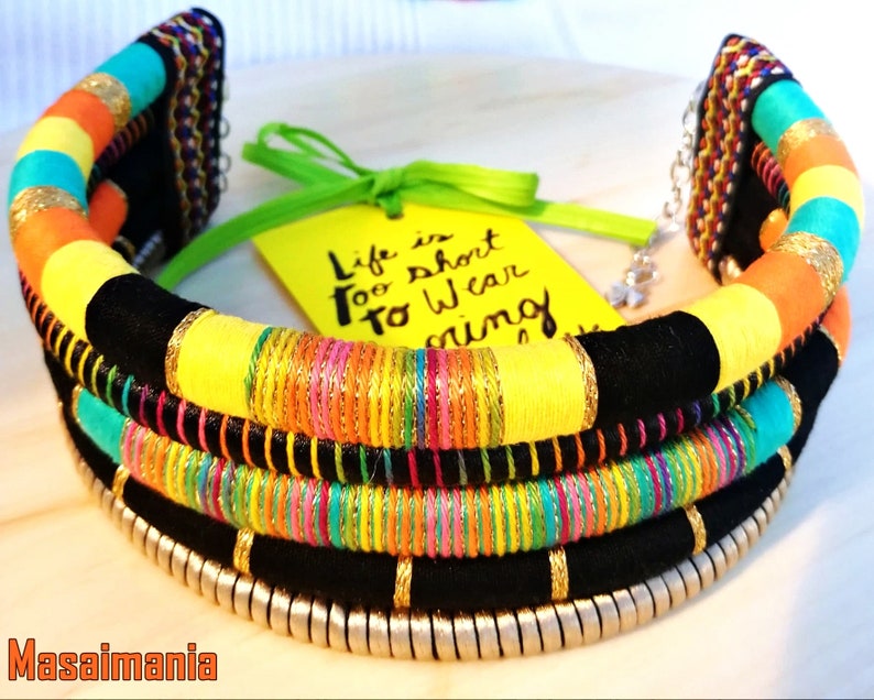 May include: A colorful multi-layered necklace with black fabric, yellow, orange, turquoise, and pink threads, and gold accents. The necklace is decorated with silver beads and has a quote card that reads "Life is short to wear boring things".