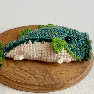 May include: A crocheted whale in blue, green, and white, displayed on a wooden plaque. The handmade whale has detailed stitching and a whimsical design, ideal for nautical-themed home decor.