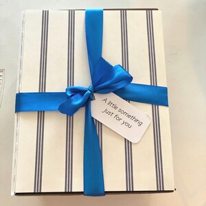 May include: A cream and navy striped gift box tied with a vibrant blue ribbon and bow. A small white tag with the words "A little something just for you" is attached to the ribbon.