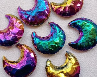 Op de afbeelding: Zeven regenboogkleurige, halve maanvormige stenen in verschillende kleuren, waaronder paars, blauw, groen en goud. De stenen zijn glad en hebben een metallic glans.