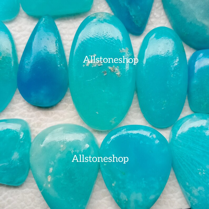 Puede incluir: Una colecci&oacute;n de cabujones turquesa, algunos de forma ovalada y otros en forma de l&aacute;grima, sobre un fondo blanco. Los cabujones tienen una apariencia transl&uacute;cida y vidriosa. El texto "Allstoneshop" aparece dos veces en la imagen.