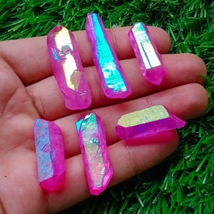May include: Seven iridescent pink and blue crystal points with a rainbow effect. The crystals are arranged in a hand, with the points facing upwards.